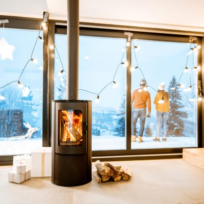 Couple standing outdoors on the terrace of the house with fireplace during the winter time. Interior view through the window