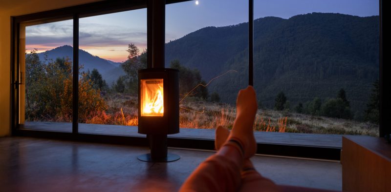 Woman resting near fireplace at modern house with great view on mountains at sunset. Women's legs on background of landscape